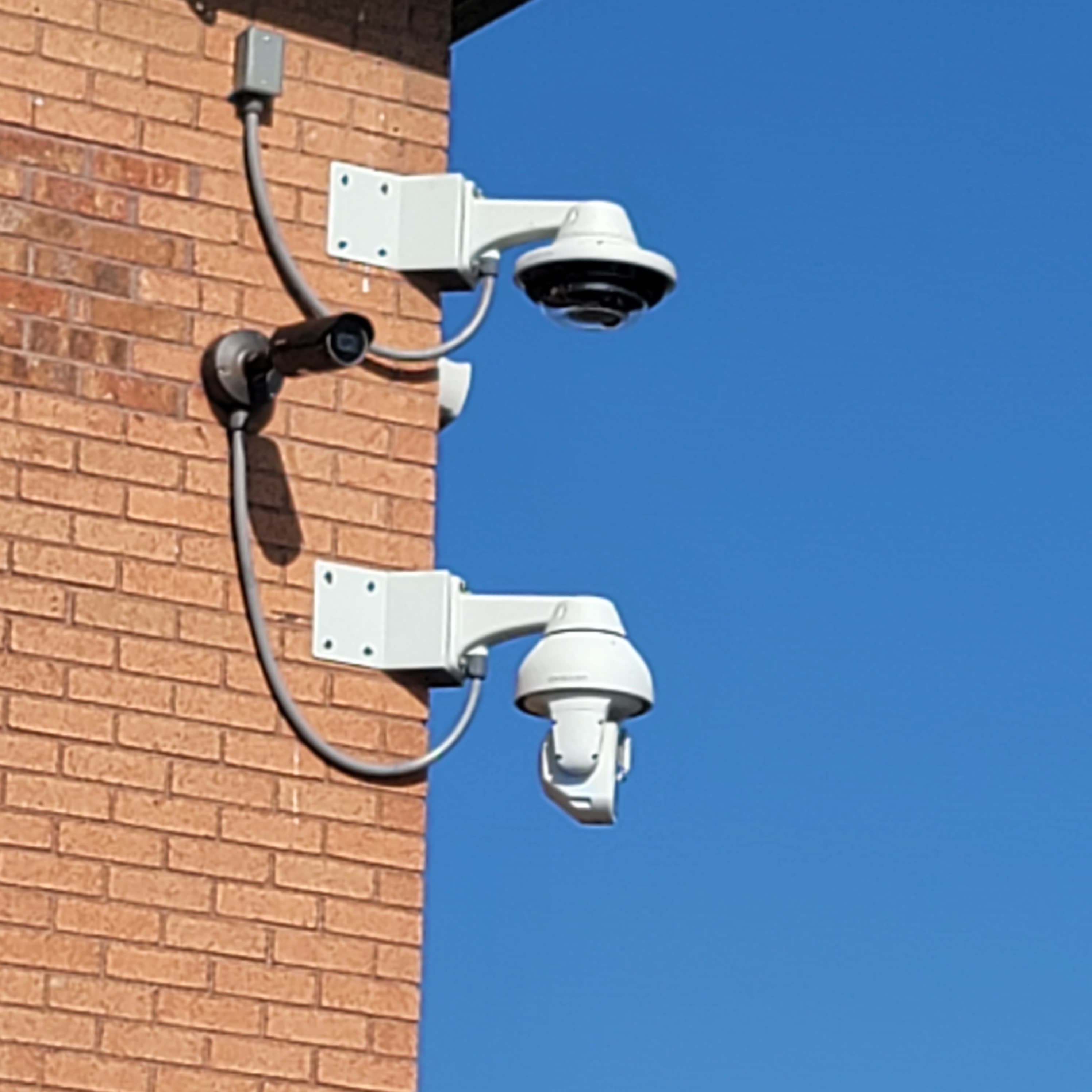 Two white dome cameras and one black bullet camera mounted on a brick wall corner.