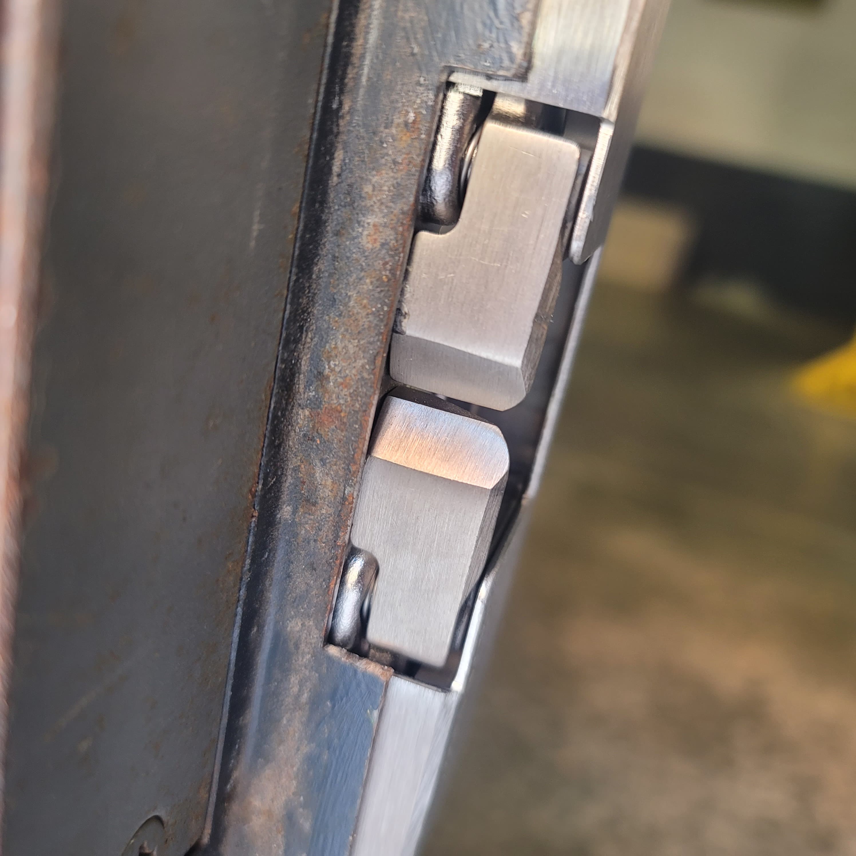 Close-up of two brushed steel latch components recessed into a dark, weathered metal frame.
