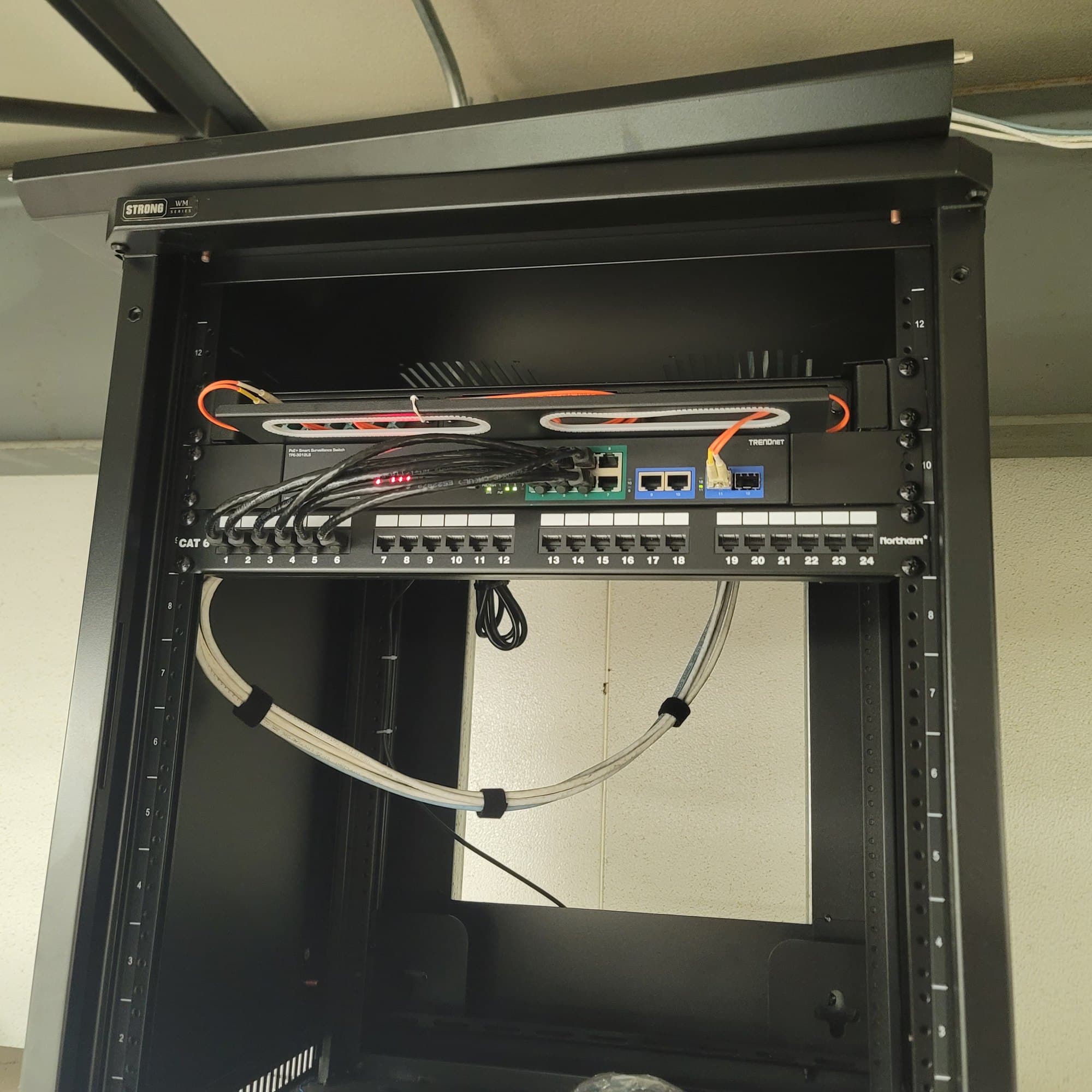 Black server rack housing a network switch and 24-port patch panel with organized ethernet cables.