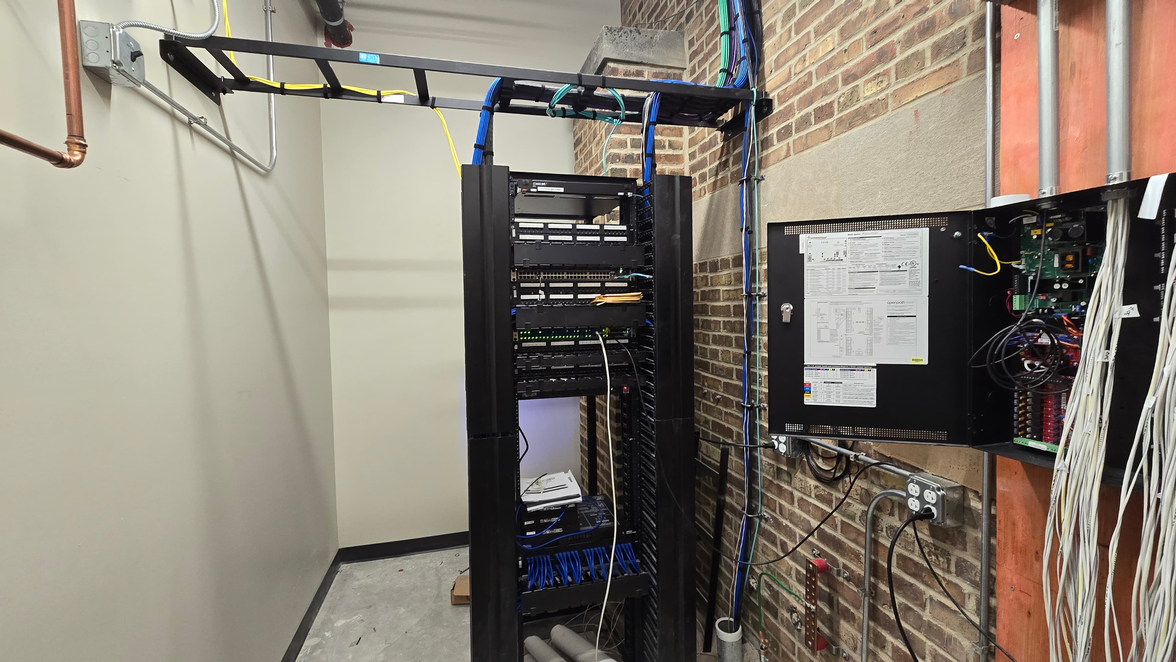 Server rack with blue cables and an open control panel against a brick wall.