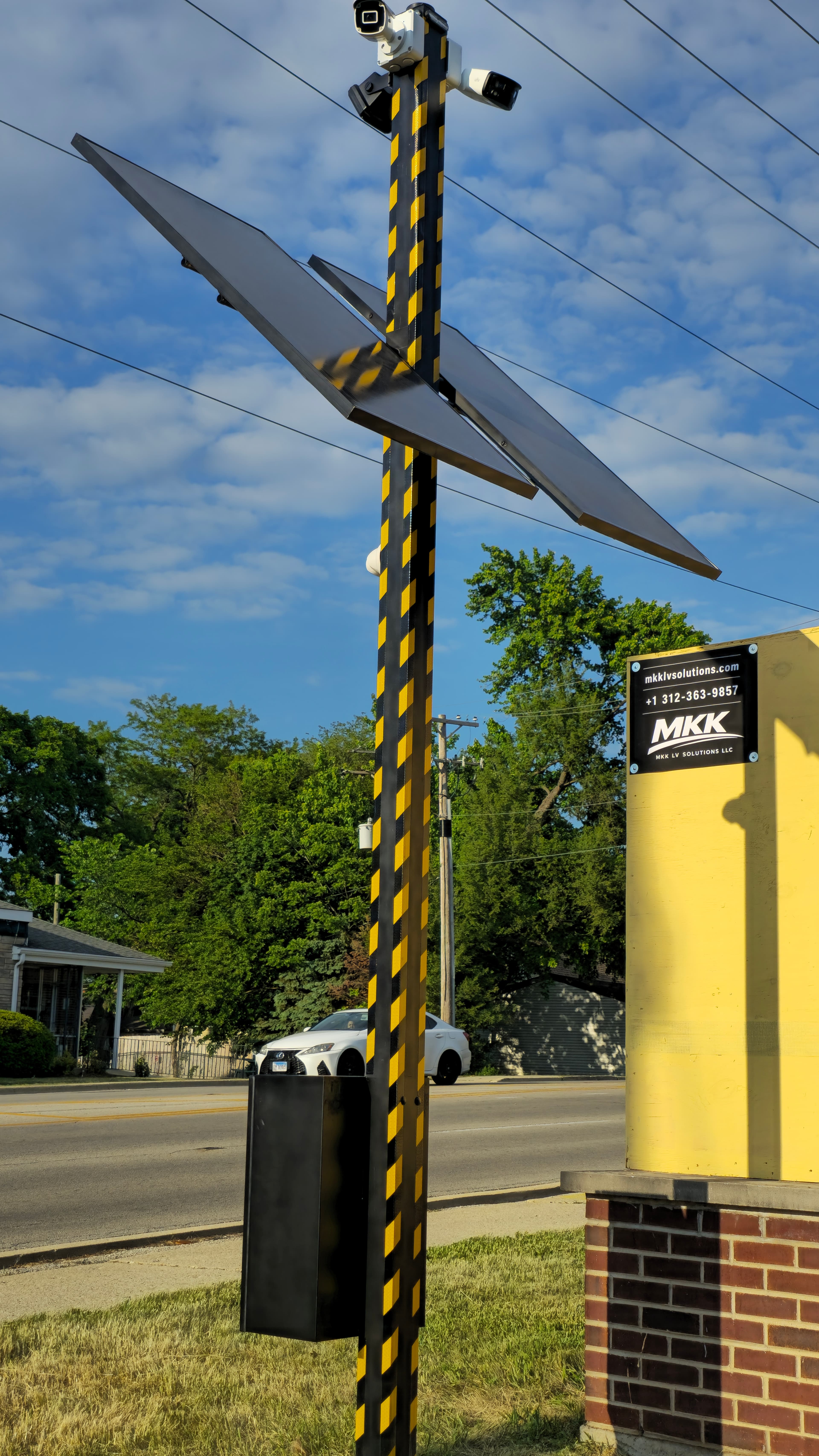 Solar-powered security pole with hazard stripes, cameras, and solar panels against a blue sky.