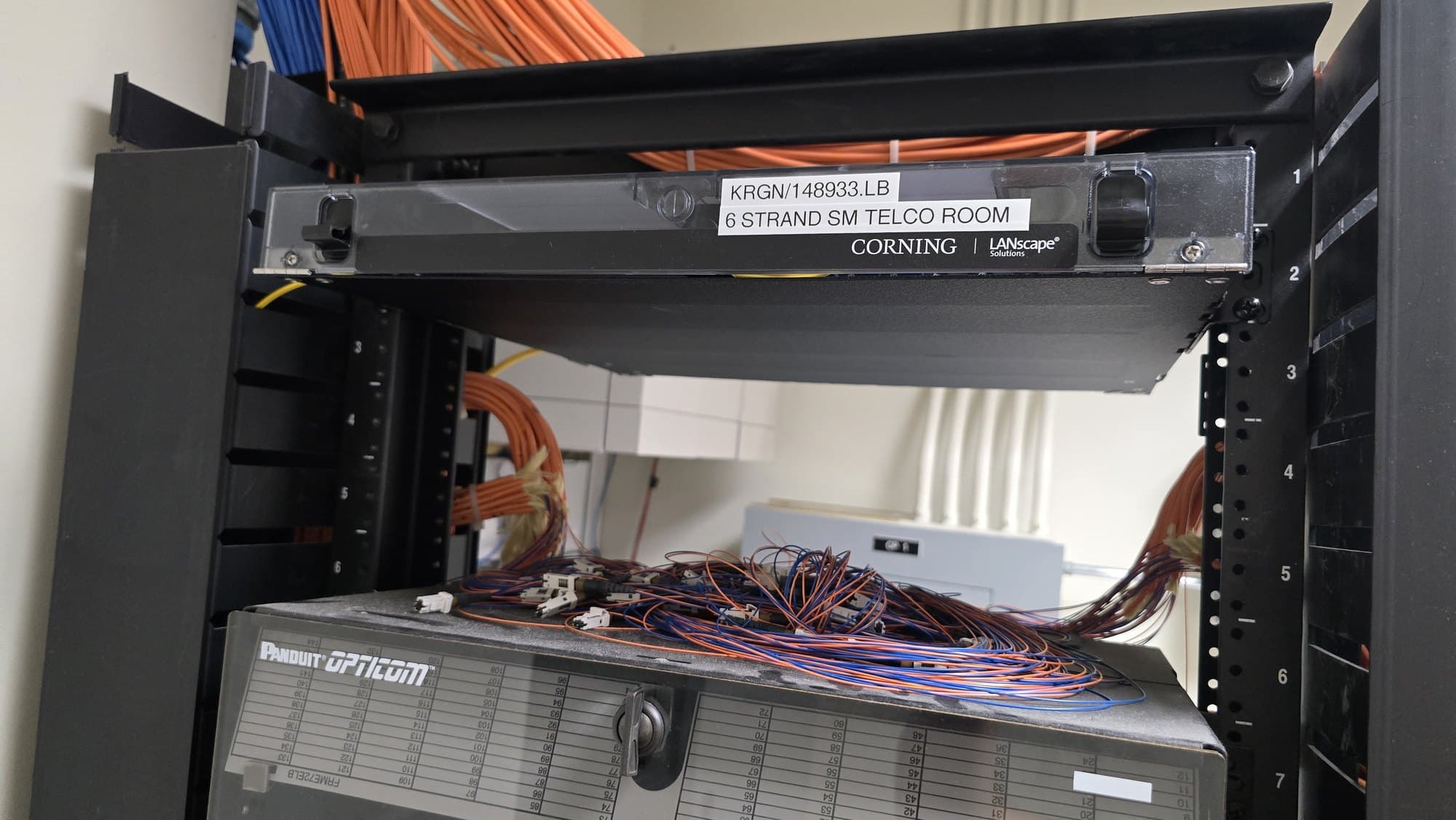 Corning fiber optic patch panel above tangled blue and orange cables in a server rack.