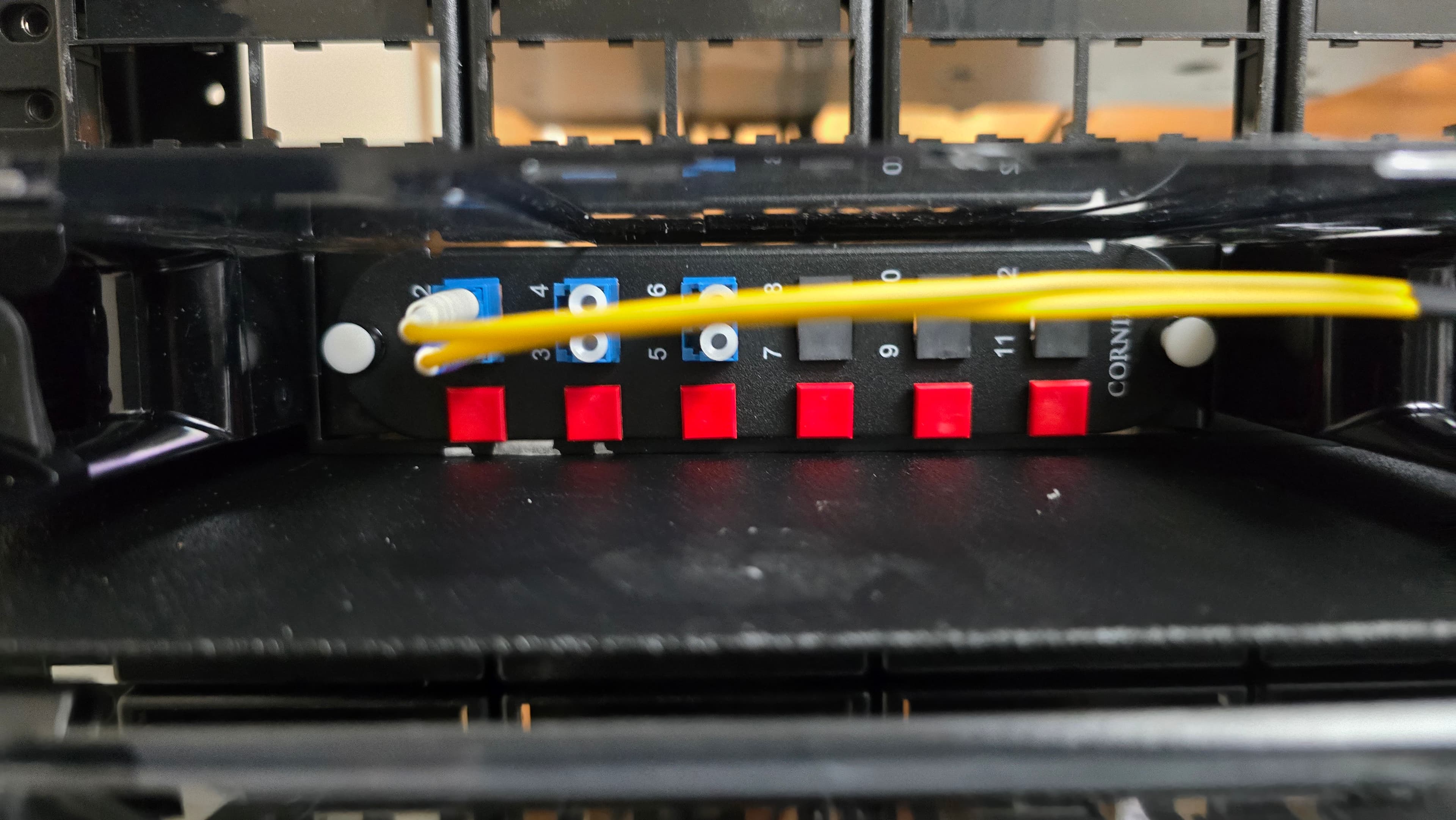 Yellow fiber optic cables connected to a black patch panel with blue ports and red caps.